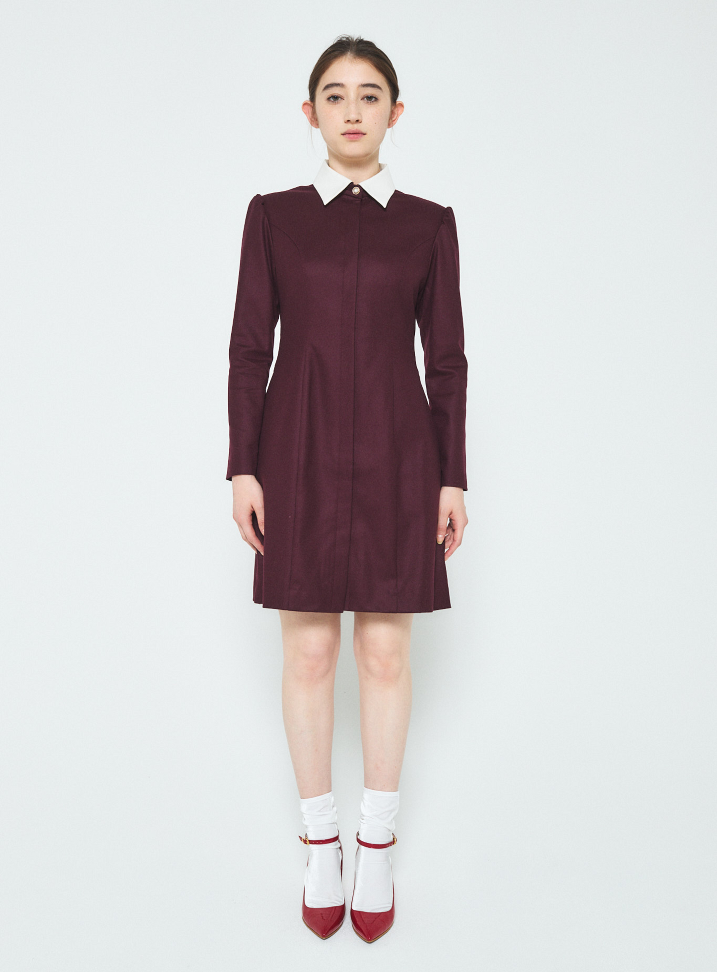 Woman wearing a burgundy dress with a white collar on a white background